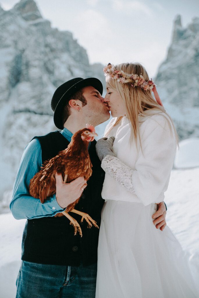 Elopement Hochzeit Paket in den Dolomiten – Paar küsst sich mit einem Huhn im Arm