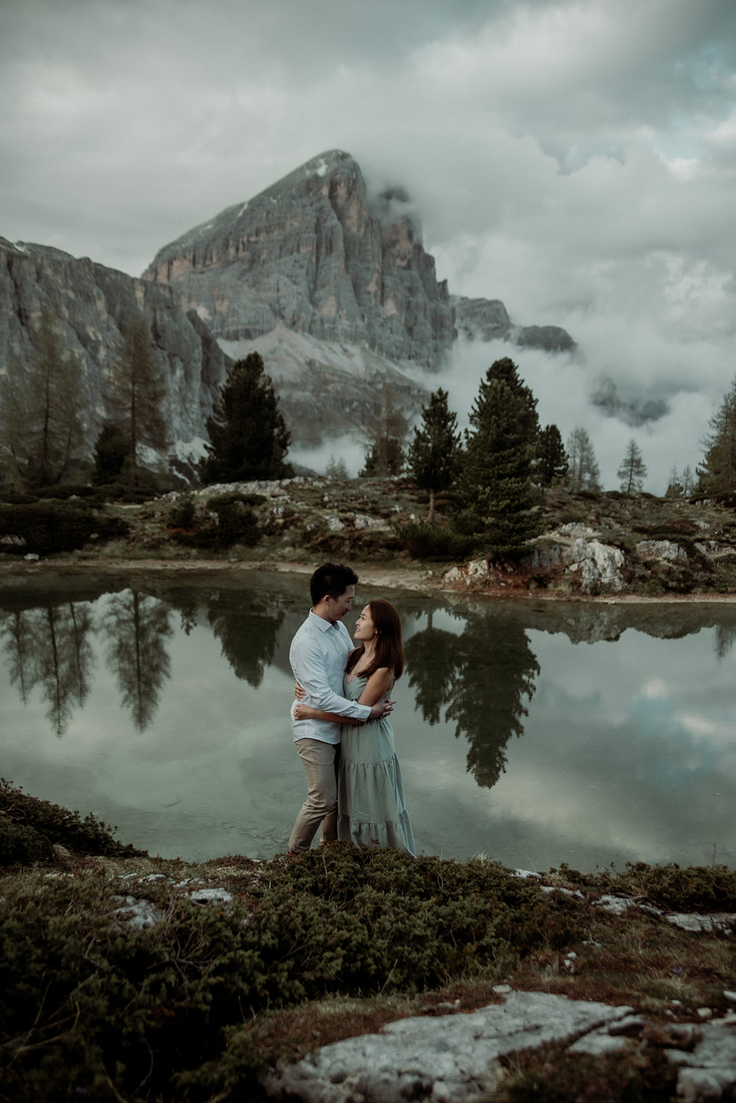 Dolomites engagement photographer - couple holding each other after the proposal in front of a lake with mountains and mist in the background